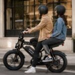 Casal com capacetes em bicicleta elétrica preta com banco para garupa