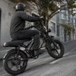 Bike elétrica preta subindo rua inclinada em cenário urbano