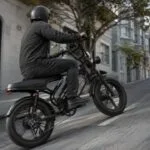 Bike elétrica preta subindo rua inclinada em cenário urbano